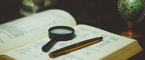 An open book with a magnifying glass and a pen