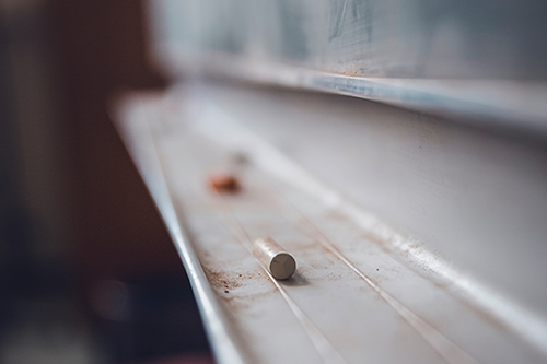 A photo of a blackboard tray with several pieces of chalk. The tray is showing a lot of use.