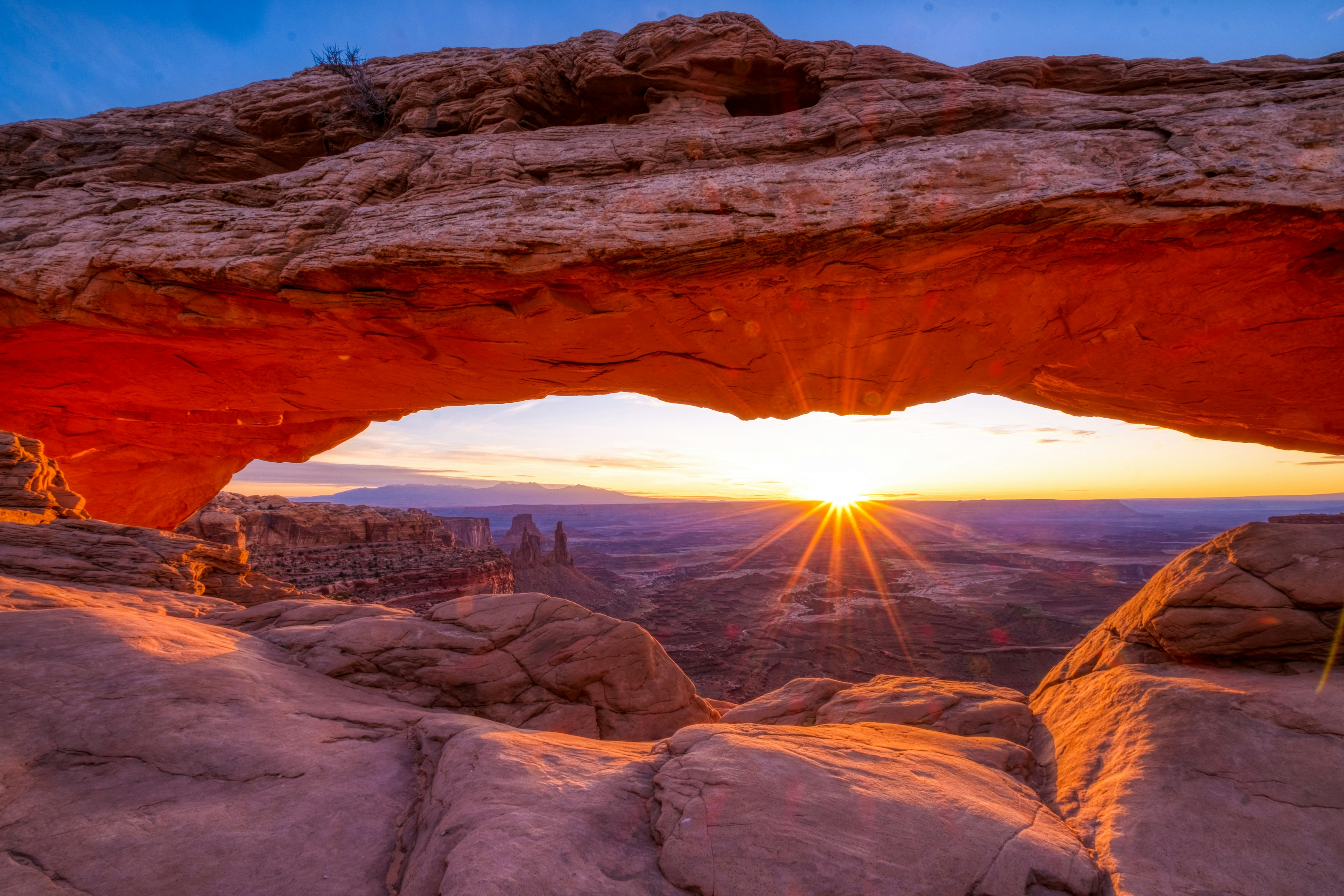 The sun rising through a rock arch in the desert.