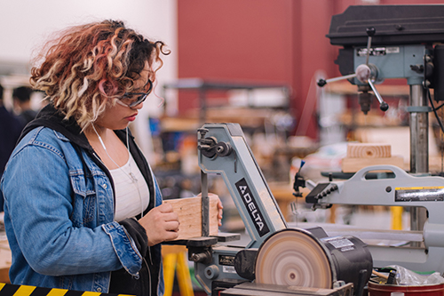 A woman using a stationary belt sander in a workshop